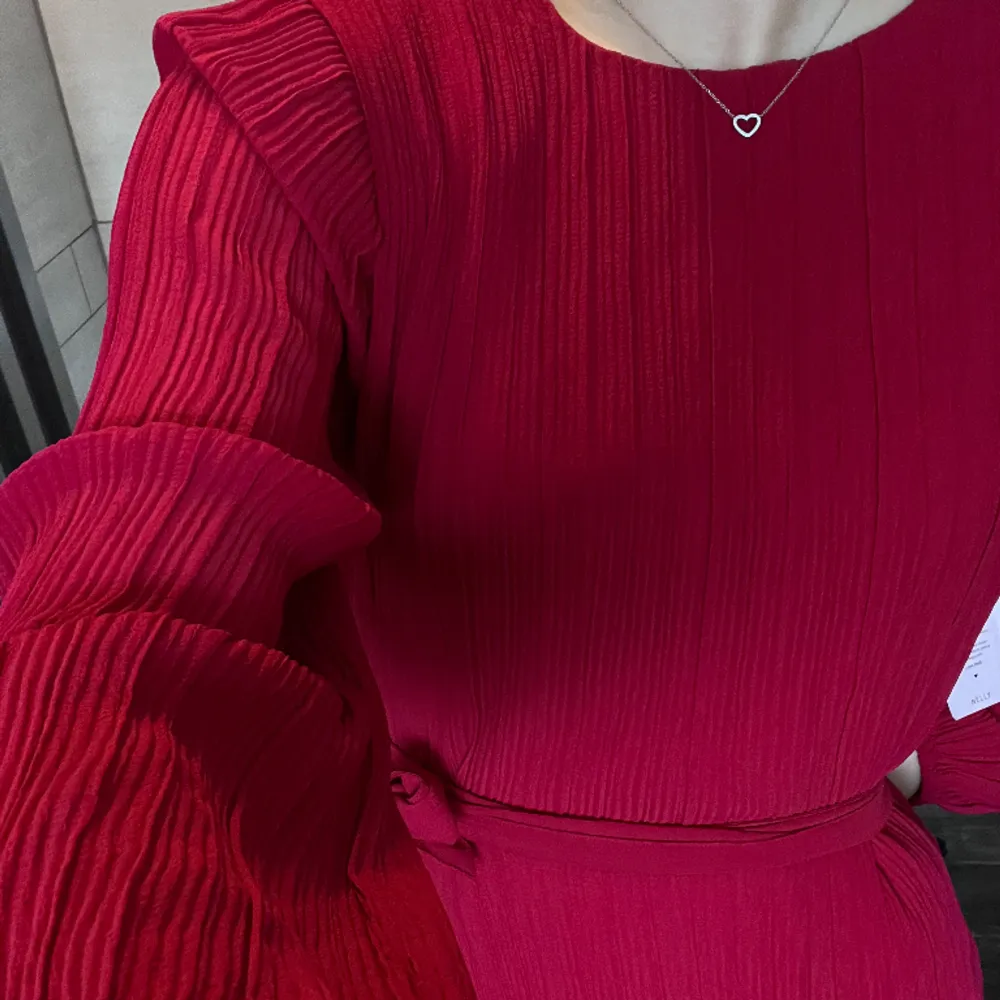 Härlig röd långärmad klänning med plisserat tyg, midjeband och puffiga ärmar. Plaggets längd är 86 cm (från axelsömmen till fållen) och klänningen slutar strax ovanför knäna. Aldrig använd och lapparna sitter kvar. Storlek 36 ❤️. Klänningar.