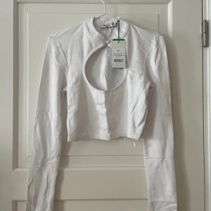 Topp från NA-KD  - Långärmad croppad vit topp från NA-KD i storlek M. Öppen vid bröstet. Aldrig använd. Ny med prislappar. Liten fläck på ärmen, har inte försökt att ta bort den. Bara att fråga om det är något du undrar! Kan mötas på Järntorget i Göteborg eller skicka