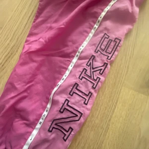 rosa nike track pants💗 - Säljer dessa snygga byxor från Nike i strl XS💕 såå snygga🪩 köpte de från plick men har endast testat de, säljer för att de var för korta i benen på mig som är 172 cm🩷 skriv för frågor! Pris kan alltid diskuteras