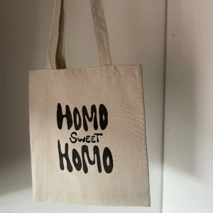 Tygkasse, tygväska, tygpåse  - Handsydd tygkasse med motivet ”homo sweet homo”.   Tillverkad i 100% återvunna textilier. Motivet är handmålad med textilfärg.   Mått: 32x35 cm  Hämtas på Södermalm alternativt skickas med post. 