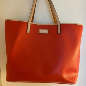 Coach tote bag park metro väska - Väska i äkta läder från Coach, modell park metro. Färgen är korall. Väskan är i mycket bra skick, inga synliga tecken på slitage (se bilder).   Mått: Höjd 30 cm Bredd 35 cm Djup 15 cm. Väskan kommer från ett djur- och rökfritt hem. Väskan har inga sk