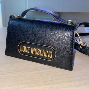 Love Moschino väska - Väskan är använd max 3 gånger så nästan i nyskick, axelbandet är juster och avtagbart. Väskan är äkta och beställd på zalando. Nypris cirka 2000kr