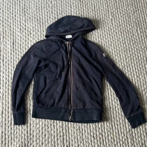 Moncler Hoodie - Fin Moncler-hoodie som säljes då jag växt ur den! Koftan är använd och därför tillkommer några flaws, därav det lägre priset. Den är köpt på HighendMarkets. 