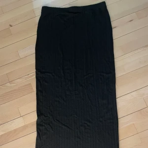 Lång svart kjol - Lång kjol i viskos/elastin. Resår i midjan o stretchig tajt modell. Långrandigt ”mönster”