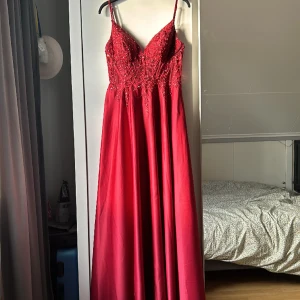 Balklänning  - En vinröd balklänning med uringning och justerbara band, små pärlor upptill och vaddering vid bystet. Endast använd en gång, väl omhändertagen.   Fri frakt. (Nypris 2 132kr) För mer information skriv till mig :)