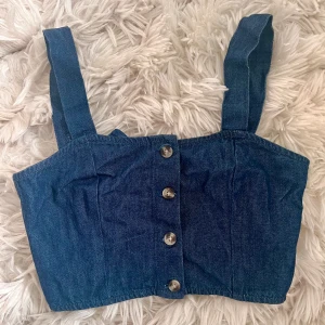 Crop top - Kort jeanstopp med knappar och justerbara band för att göra kortare eller längre. 