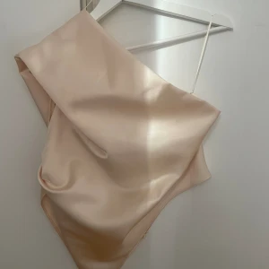 One shoulder topp  - Så fin beige one shoulder topp i satin, från zara. Knäppningen är trasig men går lätt att fixa eller så kan man sätta ihop tröjan med en säkerhetsnål! 