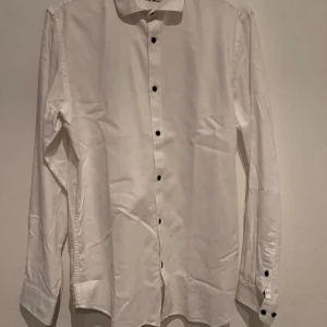 Vit sommar skjorta - En luftig och härlig sommar-skjorta med blommigt mönster i nacken och manschetten. 