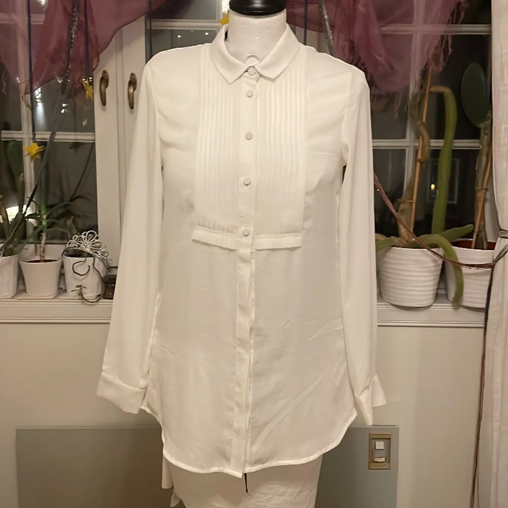 Säljer denna vita veckade skjortan med svarta knappe vid ärmarna. Den har en liten fläck vid armhålan (sista bilden) men annars är den i bra skick!. Skjortor.