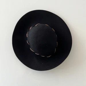 Svart Åhléns hatt  - Den är i ett väldigt bra skick och har många ljusa år i horisonten. Den har en bronskedja som cirkulerar hattens mitt. Denna hatt är ett exempel på Åhléns attraktiva designer, de visar att de är en av de bästa klädesmärkena i Norden