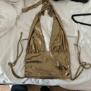 Guldig halterneck topp - Säljer en snygg guldig halterneck topp. Den är ärmlös och har en knytning i nacken. Perfekt för festliga tillfällen! ✨