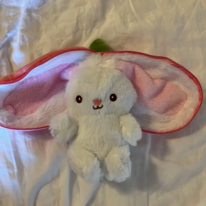 Söt vit kaninmössa med rosa insida och morotsfodral - Säljer ett supergulligt Kanin gosedjur med jordgubb fodral.  Jättemjuk och liten och är perfekt om man vill ha nåt och gosa med. har aldrig varit använt har bara legat i en låda💕