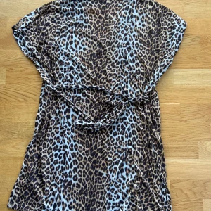 Leopardmönstrad topp med knytband - Säljer en snygg leopardmönstrad klänning med korta ärmar och knytband i midjan. Perfekt för en cool och avslappnad look. Toppen är i ett mjukt och bekvämt material.