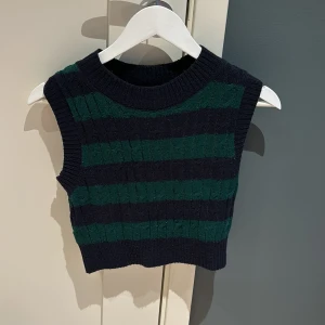 Randig stickad väst - Säljer en superfin stickad tröja/väst i storlek S. Den är randig i mörkblått och grönt och har en croppad passform. Perfekt för höst och vinter, och kan stylas över en skjorta eller t-shirt för en snygg lager-på-lager-look. Västen är i nyskick och väldigt bekväm att ha på sig. Passar både till vardags och fest!