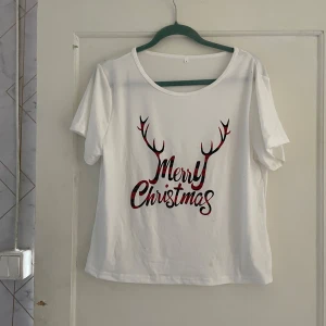 Vit jultröja med Merry Christmas-tryck - Säljer en vit t-shirt med ett festligt Merry Christmas-tryck i rött och svart. Perfekt för julfirandet! Tröjan är kortärmad och gjord av mjukt material. Passar bra till både vardag och fest under julen. 🎄