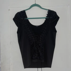 Svart topp från Finejo - Säljer en elegant svart topp från Finejo. Toppen har vackra spetsdetaljer längs framsidan och en smickrande passform. Perfekt för festliga tillfällen eller en utekväll. Toppen är i nyskick och redo att bäras!
