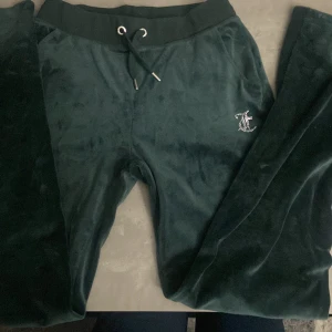 Mörkgröna mjukisbyxor från Juicy Couture - Säljer ett par mörkgröna mjukisbyxor från Juicy Couture i storlek S. Byxorna är supermjuka och bekväma, perfekta för chill dagar hemma. De har en snygg snörning i midjan och är dekorerade med glittriga stenar som bildar Juicy-loggan både fram och bak. Passar perfekt för höst och vinter när man vill vara både varm och stylish. 🖤
