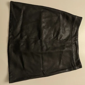 Svart kjol i läderimitation  - Svart kjol i läderimitation med dragkedja på sidan, använd fåtal gånger och är därför i mycket bra skicka! 