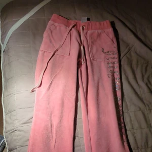 Rosa mjukisbyxor med strassdetaljer - Ett par rosa mjukisbyxor från Juicy Couture med strassdetaljer längs ena benet.  och fickor både fram och bak.
