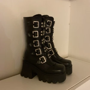 Kängor med platå och spännen - Säljer mina Demonia-liknande kängor med nitar och spännen. De har använts sparsamt men en bit av spännet har åkt av från båda skorna (3:de bilden) Köpta från Amazon för 700kr.  Innermått: ca 22,5 cm. Pälsdjur finns i hemmet! 🐾