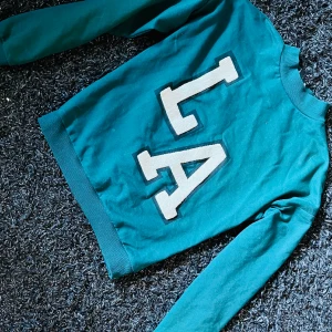 LA College tröja - Grön och fin kortare college tröja med LA text. Mellan hög krage och i gått skick. 