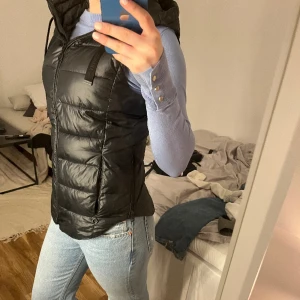 Svart dunväst - Svart dunväst med luva, som går att ta av.  I väldigt bra skick Stor i storlek skulle säga att den är S och inte XS.  Jag är 170 cm och den passar perfekt på mig som vanligtvis brukar ha storlek S.