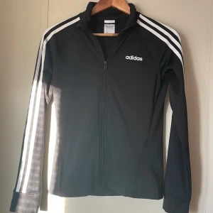 Träningsjacka adidas - En tunn träningsjacka från adidas med dragkedja och två fickor. Skönt material och jättefint skick då jag endast använt ett fåtal gånger. Storlek XS men passar även passar S💗 Kan säljas tillsammans med adidastightsen(i min profil) för ett lägre pris☺️