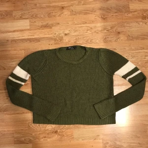 Stickad skön mjuk tröja  - Snygg grön långärmad tröja med vita ränder på ärmarna. Kort modell mjuk och skön och ganska tunn. 