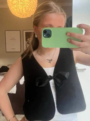 Svart väst med rosett från Monki - Fin svart Lurv väst med ett siden band, jätte fin över en outfit 