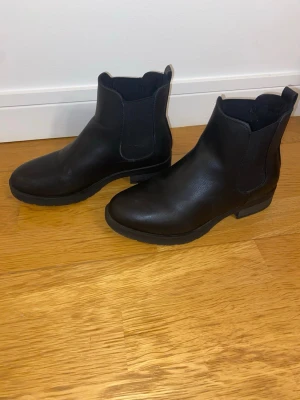 Svarta Chelsea boots i skinn - Stilrena svarta Chelsea boots i äkta skinn med klassisk resår på sidorna och låg klack. Perfekta för dig som vill ha en tidlös och enkel look. Dragflik bak för enkel påtagning. Passar till det mesta och ger en clean vibe.
