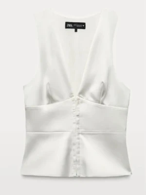 Vit v-ringad linnetopp från Zara - Stilren vit linnetopp från Zara med djup v-ringning och knappar framtill. Toppen har en figurnära passform och är ärmlös, vilket gör den perfekt för varma dagar. Materialet har en lätt glansig finish som ger en exklusiv känsla.