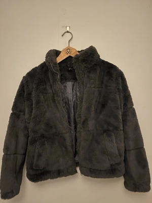 Mörkgrå teddyjacka från New Look - Säljer en fluffig och trendig mörkgrå teddyjacka från New Look. Jackan har hög krage, dragkedja framtill och två stora fickor. Perfekt för att hålla sig varm och snygg under kyliga dagar. Materialet är mjukt och gosigt, vilket ger en riktigt cozy vibe. Aning liten i storlek, så ungefär 36/38. Jackan är i storlek 38, men känns mer som 36. Dragkedjan är lite trög, därav lägre pris. Nypris 500kr