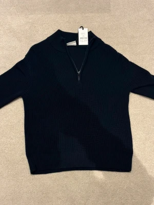 Svart stickad tröja med halv dragkedja - Svart stickad tröja från Gina Tricot med ribbad struktur och halv dragkedja framtill. Tröjan har hög krage och långa ärmar, vilket ger en clean och stilren look. Perfekt att bära över en t-shirt eller skjorta.