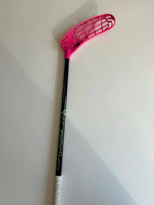 OXDOG innebandyklubba svart/rosa - Innebandyklubba från OXDOG med svart skaft och ett rosa blad i plast. Skaftet har text och detaljer i grönt och vitt, samt ett vitt grepp längst ner. Klubba nästa helt ny, bladet är ändå bra. Avox blad och hyperlight klubba, klubban 98cm lång