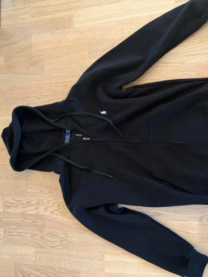 Svart zip up hoodie från Polo Ralph Lauren - Svart hoodie från Polo Ralph Lauren med dragkedja och två fickor på framsidan. Hoodien är helt ny och har endast testats. Den är egentligen en L men storleken är liten och passar mer en M 