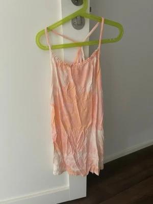 Pastellfärgat linne med smala band kan också vara klänning - Sött linne i pastellrosa och vitt med tunna axelband och avslappnad passform. Materialet ser ut att vara mjukt och lätt, perfekt för varma nätter. Ingen synlig logga eller märke. Färgen har en tie-dye känsla och linnet har en enkel, ungdomlig stil.