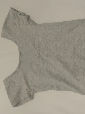 Grå basic croptop backless - Enkel och stilren grå t-shirt med rund backless ringning och korta ärmar. Perfekt att matcha med jeans eller kjol för en avslappnad look. Tillverkad i mjukt bomullsmaterial som känns skönt mot huden.
