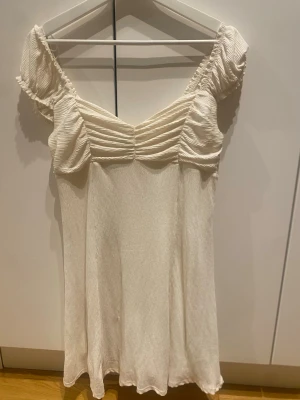 Ljusgul  kortklänning från Gina Tricot - Supersöt ljusgul  kortklänning från Gina Tricot med puffiga kortärmar och rynkade detaljer över bysten. Klänningen har en lätt struktur i tyget och en luftig känsla, perfekt för varma dagar. Passar dig som gillar en feminin och trendig stil.