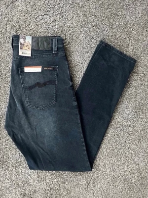 Mörkblå slim fit jeans från Nudie - Snygga mörkblå slim fit jeans från Nudie Jeans med klassisk femficksdesign och subtila slitningar framtill. Jeansen har en broderad bakficka och är tillverkade i mjuk, stretchig denim för extra komfort. Perfekta för en avslappnad och trendig look. Storleken är 31/34 men de sitter mindre som 30/32