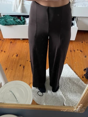 Bruna vida leggings med söm - Säljer ett par bruna leggings med vida ben och markerad söm framtill. De har hög midja och är tillverkade i ett stretchigt material som sitter bekvämt. Perfekta för en avslappnad men ändå trendig look.