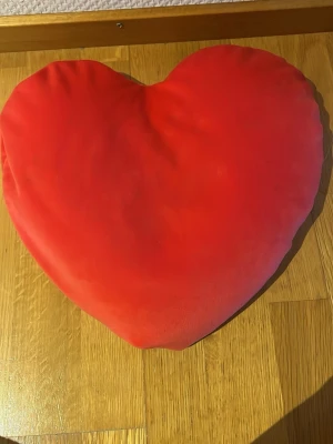 Rött hjärtformat kuddfodral - Mjuk kudde i form av ett hjärta med stark röd färg. Kudden har en slät yta och är tillverkad i ett sammetsliknande tyg. Perfekt som dekoration i soffan eller på sängen för en mysig vibe.