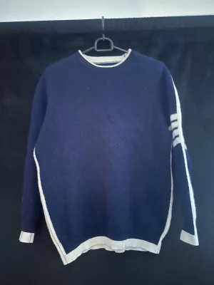 Axel luxe - Snygg marinblå stickad tröja med vita ränder på ena ärmen och vita kanter vid hals, ärmslut och nederkant. Tröjan har rund halsringning och en avslappnad passform. Perfekt för dig som gillar klassisk men sportig stil.