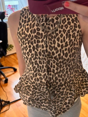 Leopardmönstrad ärmlös blus - Snygg ärmlös blus med leopardmönster och volang nertill. Blusen har knytning framtill och en lätt, luftig känsla. Perfekt för dig som vill sticka ut med ett djurmönstrat plagg.