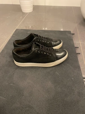 Svarta sneakers med vit sula - Svarta sneakers med vit sula och snörning. Ovandelen är i mocka och skinn, med blanka detaljer på tån och matta sidor. Klassisk låg modell med rund tå och metallöljetter. Perfekta för en clean och stilren look. (vid frågor är det bara att ställa) storlek är i UK 10. Dem är i väldigt bra skick 