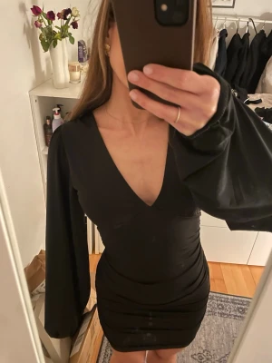 Miniklänning med v-ringning  - Snygg svart kort klänning med tight passform och v-ringning, med ballongärmar! Scrunch i sidan som gör att den sitter snyggt☺️ Endast använd 2 gånger!!!