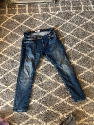 Blå slim fit jeans från H&M - Snygga blå slim fit jeans från H&M med klassisk femficksdesign och lätt slitna detaljer framtill. Jeansen har normal midja och smala ben, perfekta till en avslappnad stil. Tillverkade i bomull med lite stretch för extra komfort.