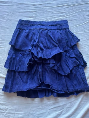 Blå volangkjol med resårmidja - Supersöt blå kortkjol med flera lager volanger och bekväm resår i midjan. Storlek 0 vilket motsvarar Xs