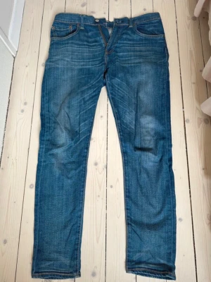 Blå Levi's jeans med raka ben - Säljer ett par klassiska blå jeans från Levi's med raka ben och fem fickor. Jeansen har snygga slitningar och en ikonisk läderpatch bak i midjan. Tillverkade i bomull med en autentisk denimkänsla. Perfekta för en avslappnad och trendig stil.
