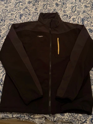 National Geographic Nordic svart jacka, storlek XL - Svart jacka från National Geographic Nordic med dragkedja framtill och en gul dragkedjeförsedd bröstficka. Jackan har en hög krage