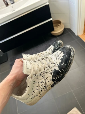 Maison Margiela - Vita Maison Margiela med mörkblått färg stänk, storlek 45 men passar bra 44. Kommer att såklart tvätta skorna noga vid köp. Tänker mig 2999kr för skorna men smidiga affärer kommer alltid med fördelar. Skorna är super fint skick Tyvär med kommer inget og mvh/ Gardefashion 